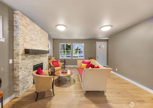 living area with baseboards, a stone fireplace, and light wood-type flooring