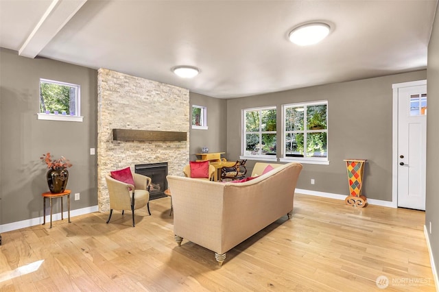 living room with light wood finished floors, a stone fireplace, and a healthy amount of sunlight