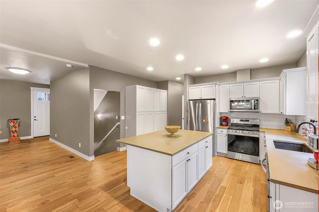 kitchen featuring light wood finished floors, a sink, white cabinetry, appliances with stainless steel finishes, and decorative backsplash