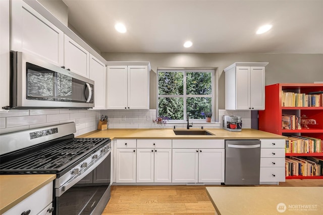 kitchen with a sink, light wood-type flooring, white cabinetry, light countertops, and appliances with stainless steel finishes