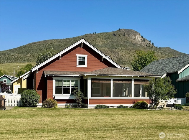 rear view of house featuring a sunroom, a shingled roof, a mountain view, and a lawn