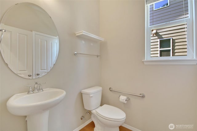 half bathroom with toilet, baseboards, and a sink