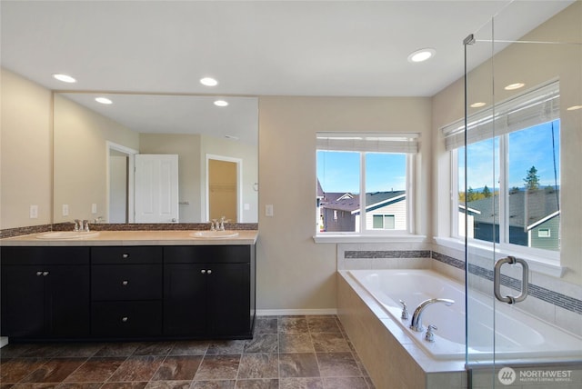 bathroom with double vanity, a garden tub, baseboards, and a sink