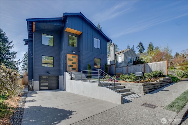 contemporary house with an attached garage, board and batten siding, concrete driveway, and fence
