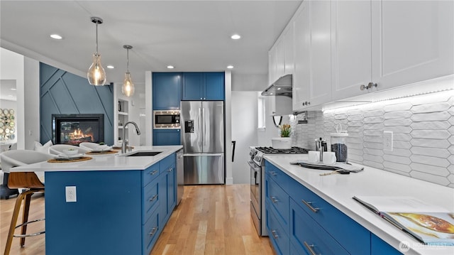 kitchen with wall chimney range hood, blue cabinets, a breakfast bar area, stainless steel appliances, and a sink