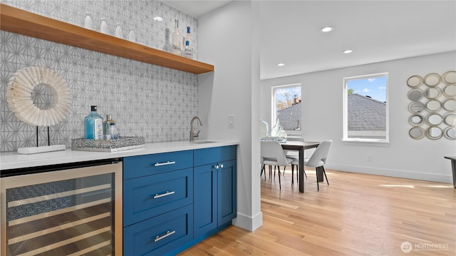 bar featuring light wood-style floors, indoor wet bar, a sink, beverage cooler, and decorative backsplash