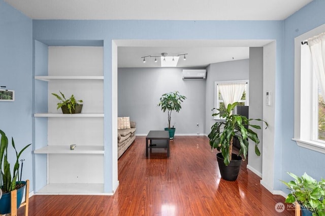 sitting room with a wall mounted air conditioner, plenty of natural light, and wood finished floors
