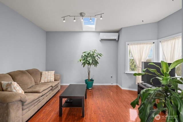 living room featuring baseboards, rail lighting, a wall unit AC, a skylight, and wood finished floors