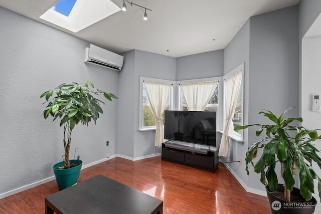 sitting room featuring baseboards, an AC wall unit, wood finished floors, and a skylight