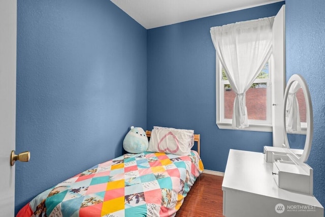 bedroom with a textured wall, baseboards, and wood finished floors