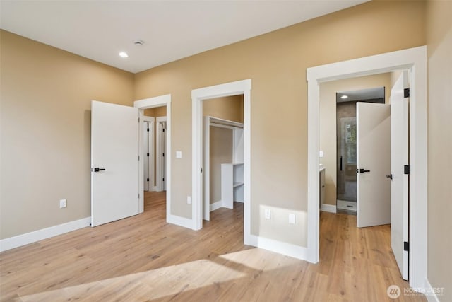 unfurnished bedroom featuring light wood-style flooring, a walk in closet, ensuite bath, and baseboards