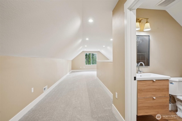 hallway with carpet floors, visible vents, baseboards, and lofted ceiling