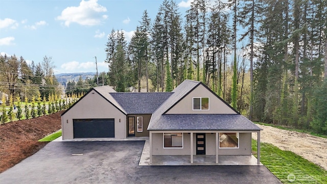 view of front of property featuring a porch, a garage, stucco siding, driveway, and roof with shingles