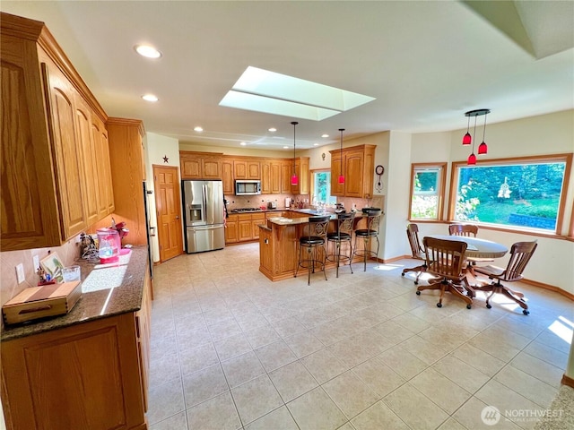 kitchen featuring tasteful backsplash, a skylight, a breakfast bar, light tile patterned floors, and appliances with stainless steel finishes