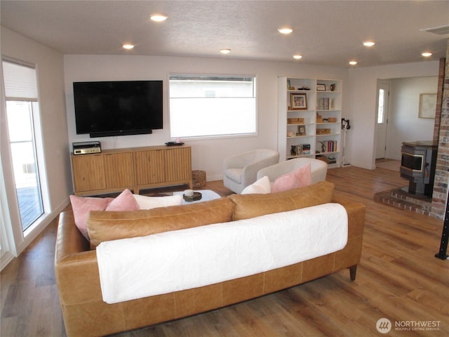 living area featuring recessed lighting, visible vents, a wood stove, and wood finished floors