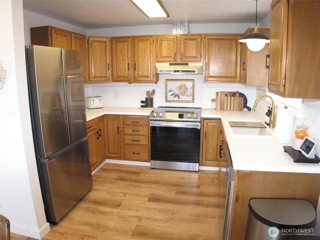 kitchen with light countertops, under cabinet range hood, light wood-style floors, appliances with stainless steel finishes, and a sink
