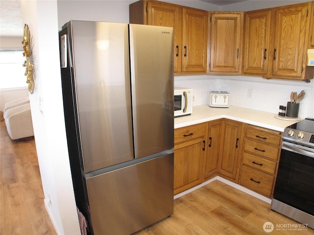 kitchen with brown cabinets, light countertops, light wood-style floors, and stainless steel appliances