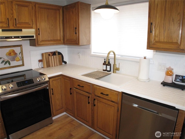 kitchen featuring appliances with stainless steel finishes, extractor fan, brown cabinets, decorative backsplash, and a sink
