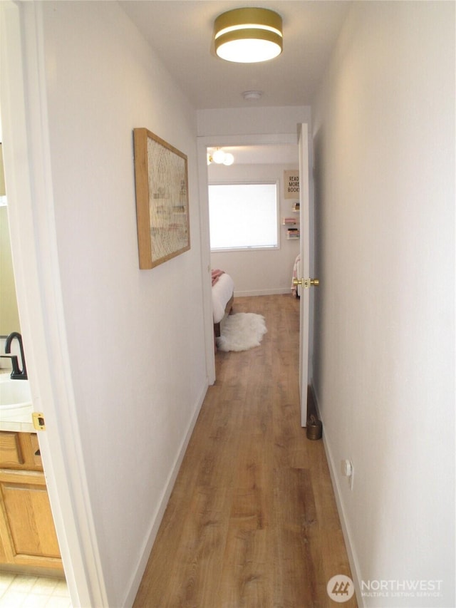 hall with a sink, baseboards, and light wood-type flooring
