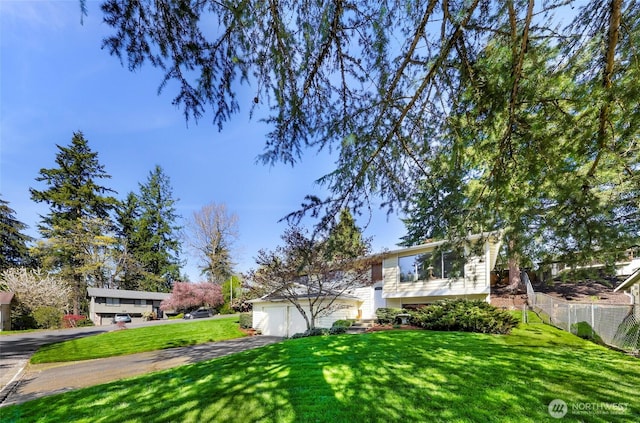 raised ranch with a garage, a front lawn, aphalt driveway, and fence