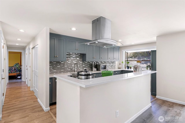 kitchen featuring decorative backsplash, light countertops, island range hood, and light wood-style flooring