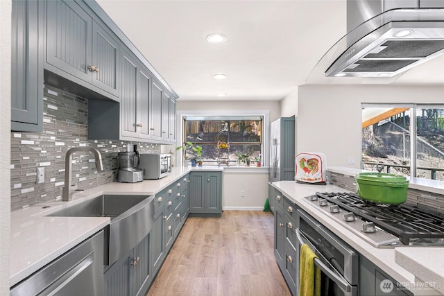 kitchen featuring stainless steel appliances, a sink, tasteful backsplash, light wood-type flooring, and wall chimney range hood