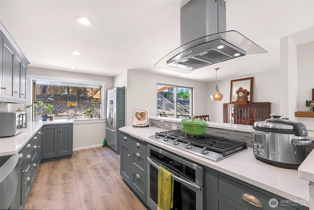 kitchen featuring island exhaust hood, light countertops, gray cabinets, light wood-type flooring, and appliances with stainless steel finishes