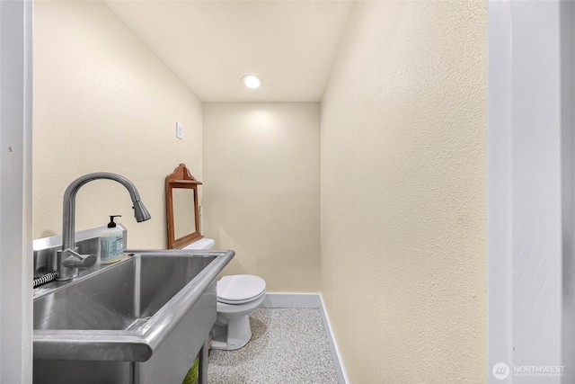 bathroom featuring toilet, baseboards, and a sink