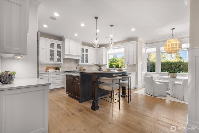 kitchen with light countertops, light wood-style flooring, white cabinetry, decorative backsplash, and glass insert cabinets