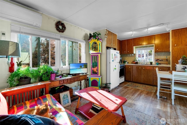 kitchen with brown cabinets, a sink, freestanding refrigerator, a wall unit AC, and light wood-type flooring