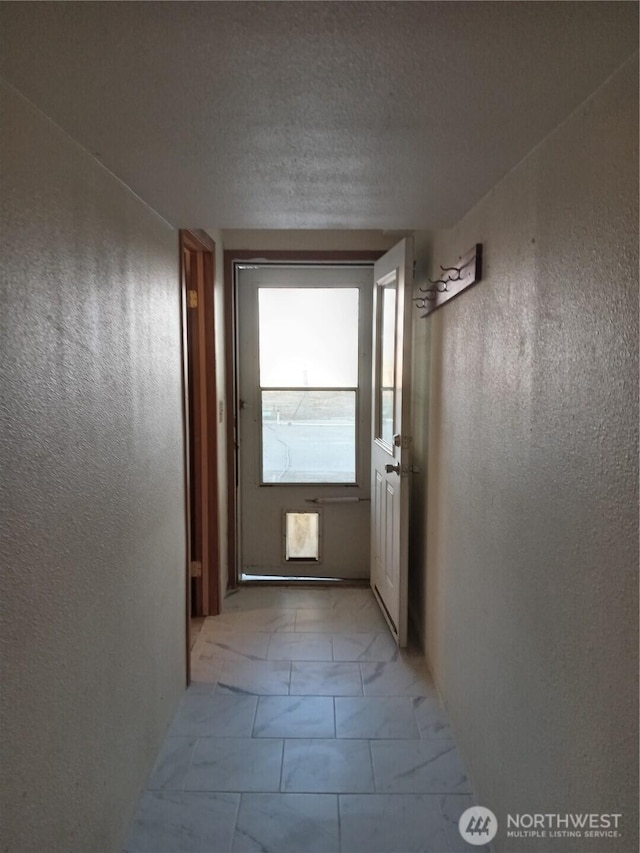 corridor featuring a textured wall and marble finish floor