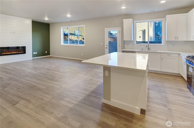 18218 37th Ave E, Tacoma, WA 98446 - kitchen with light wood-type flooring, a large fireplace, open floor plan, light countertops, and a center island