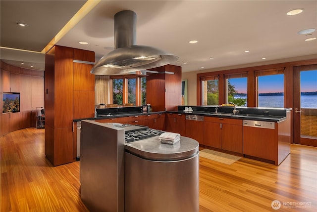 kitchen featuring a sink, light wood-type flooring, dark countertops, island exhaust hood, and paneled dishwasher