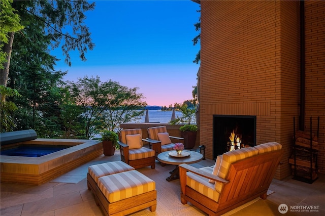 view of patio / terrace with an outdoor living space with a fireplace, an outdoor hot tub, and a water view