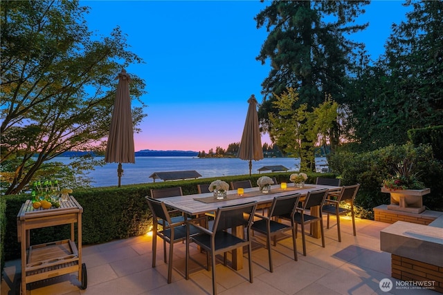 patio terrace at dusk featuring outdoor dining space and a water view