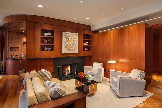 interior space featuring recessed lighting, wooden walls, a fireplace with flush hearth, built in shelves, and wood finished floors