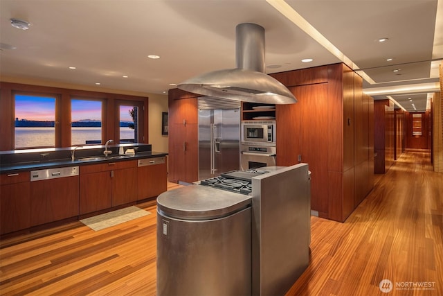 kitchen with built in appliances, modern cabinets, a sink, light wood-style floors, and island exhaust hood