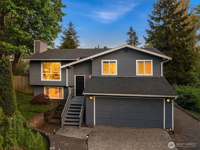 bi-level home with a chimney, a garage, asphalt driveway, stairway, and roof with shingles