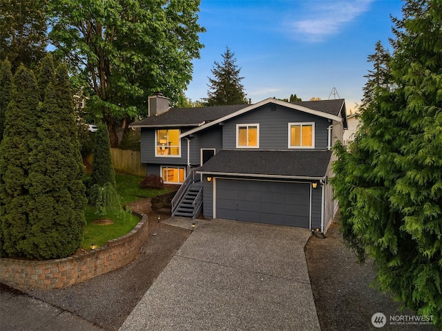 view of front of home featuring driveway, a chimney, a garage, roof with shingles, and fence