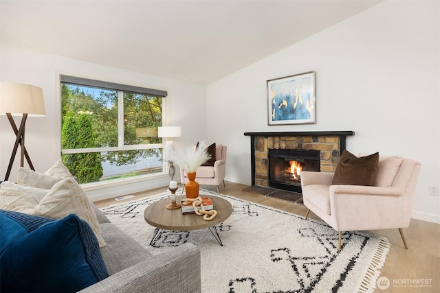 living room featuring wood finished floors, vaulted ceiling, a fireplace, and baseboards