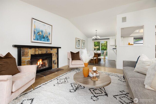 living room featuring a chandelier, wood finished floors, lofted ceiling, a stone fireplace, and baseboards