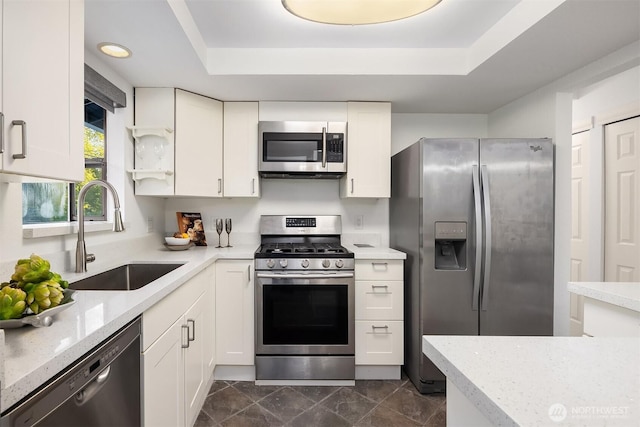 kitchen with appliances with stainless steel finishes, a sink, white cabinets, and a raised ceiling