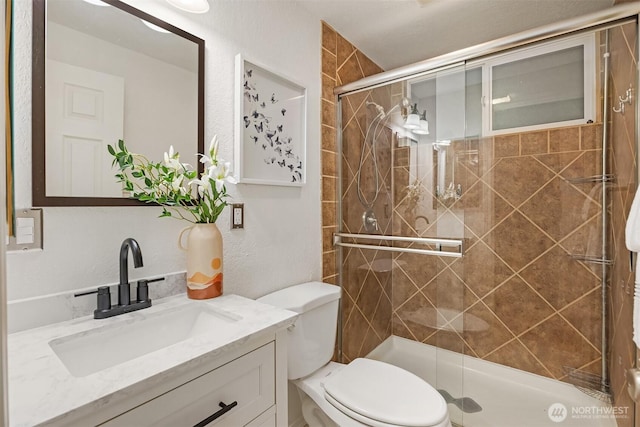 bathroom with a shower stall, toilet, vanity, and a textured wall