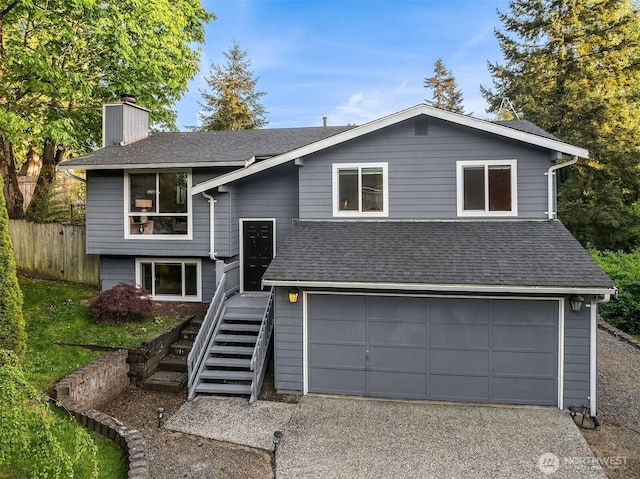 raised ranch with a chimney, fence, asphalt driveway, a garage, and a shingled roof