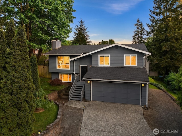 raised ranch featuring a chimney, stairway, concrete driveway, a garage, and roof with shingles
