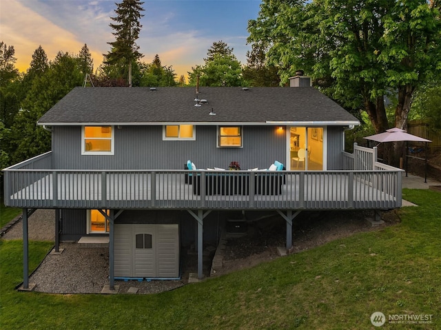 back of property at dusk featuring a deck, a yard, a chimney, and roof with shingles