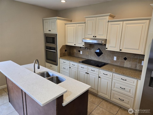 kitchen featuring a sink, light tile patterned floors, appliances with stainless steel finishes, a center island with sink, and under cabinet range hood