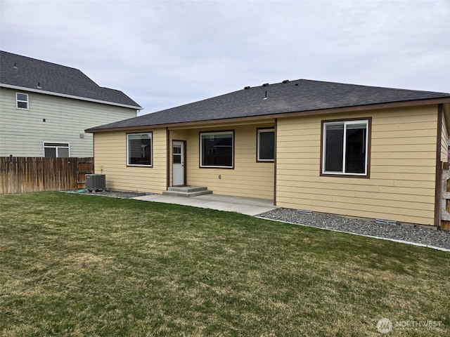 rear view of house with roof with shingles, a patio area, central AC, fence, and a lawn