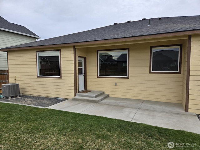 rear view of house with a patio, roof with shingles, a yard, and central AC unit