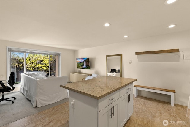 kitchen featuring open floor plan, recessed lighting, a center island, white cabinets, and light stone counters